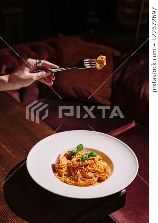 Beautifully plated pasta dish being enjoyed in a cozy dining setting with warm lighting 122672697