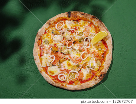 Delicious seafood pizza topped with calamari, olives, and a wedge of lemon on a green table 122672707