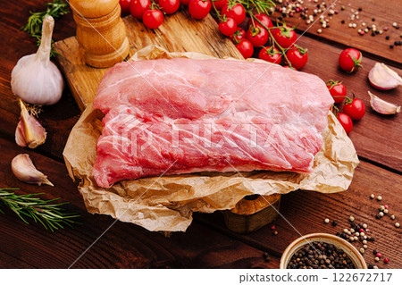 Fresh pork cut on wooden board with garlic and cherry tomatoes in rustic kitchen setting Fresh pork cut on wooden board with garlic and cherry tomatoes in rustic kitchen setting 122672717