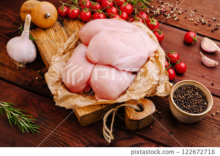 Fresh chicken breasts arranged with cherry tomatoes, garlic, and spices on a wooden table top Fresh chicken breasts arranged with cherry tomatoes, garlic, and spices on a wooden table top 122672718