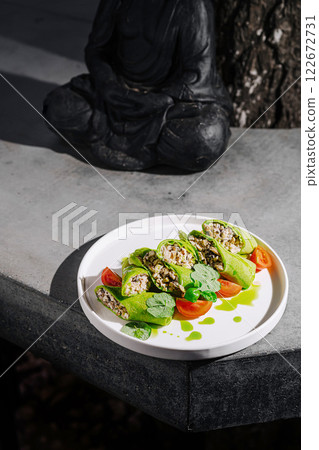Gourmet dish featuring fresh green wraps with a filling of herbs and vegetables served on a stone table beside a meditating figure Gourmet dish featuring fresh green wraps with a filling of herbs and vegetables served on a stone table beside a meditating figure 122672731