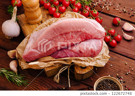 Fresh meat cuts with herbs and vegetables prepared for cooking in a rustic kitchen setting Fresh meat cuts with herbs and vegetables prepared for cooking in a rustic kitchen setting 122672748