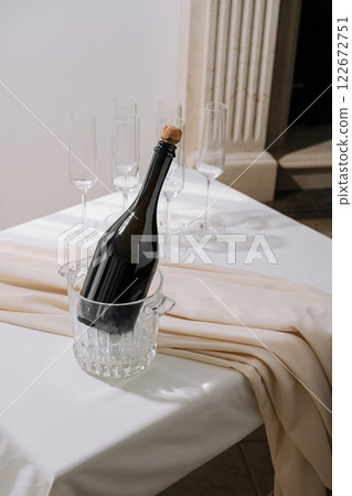 Elegant champagne bottle chilling in a crystal ice bucket with flutes beside on a white table Elegant champagne bottle chilling in a crystal ice bucket with flutes beside on a white table 122672751
