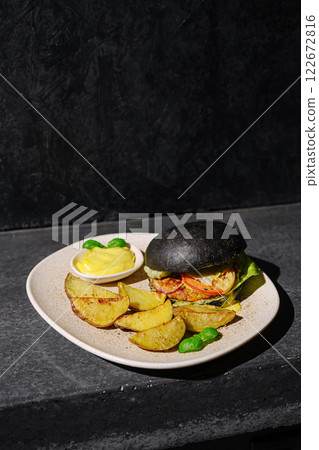 Unique black burger served with golden roasted potatoes and dipping sauce on a dark stone background 122672816