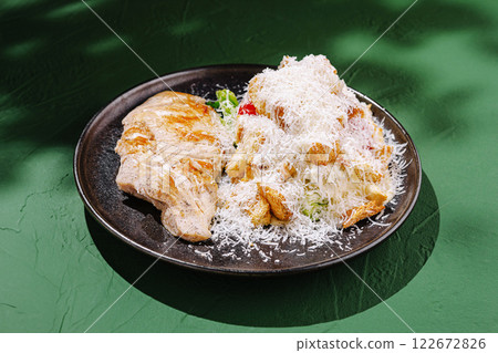 Grilled chicken served with a fresh salad topped with cheese on a black plate against a green background Grilled chicken served with a fresh salad topped with cheese on a black plate against a green background 122672826