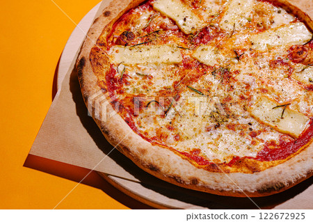 Freshly baked cheese pizza with herbs on a bright orange table ready to be enjoyed 122672925