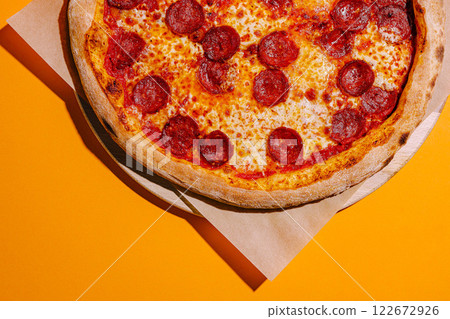 Delicious pepperoni pizza on a wooden board with a vibrant orange background Delicious pepperoni pizza on a wooden board with a vibrant orange background 122672926