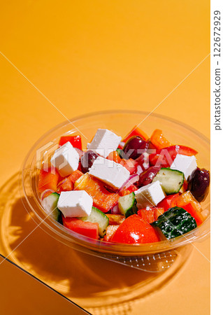 Fresh Greek salad with cucumbers, tomatoes, olives, and feta cheese on a vibrant yellow background Fresh Greek salad with cucumbers, tomatoes, olives, and feta cheese on a vibrant yellow background 122672929