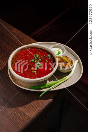 Spicy red soup served in a bowl with garnishes and sides at a cozy restaurant setting Spicy red soup served in a bowl with garnishes and sides at a cozy restaurant setting 122672939