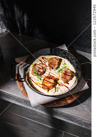 Gourmet dish featuring grilled meat served with creamy sauce on a wooden board in a modern kitchen setting 122672940