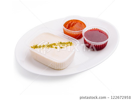 Dessert platter featuring creamy pudding with pistachios and two vibrant fruit syrups at a dining table 122672958