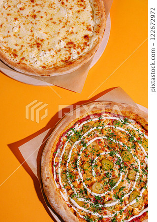 Delicious pizzas displayed on a vibrant orange background, showcasing cheese and unique toppings with fresh ingredients 122672972