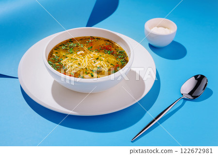 Delicious bowl of soup with herbs and noodles on vibrant blue background Delicious bowl of soup with herbs and noodles on vibrant blue background 122672981