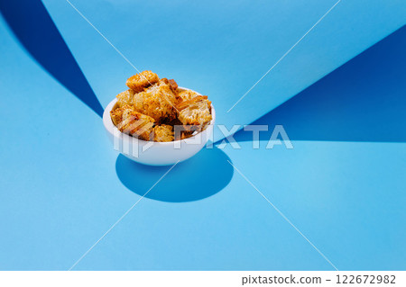 Golden crispy bread cubes in a white bowl against a blue backdrop creating visually appealing contrast Golden crispy bread cubes in a white bowl against a blue backdrop creating visually appealing contrast 122672982