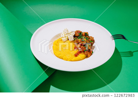 Delicious homemade polenta topped with savory stew and fresh cheese presented on a vibrant green background 122672983