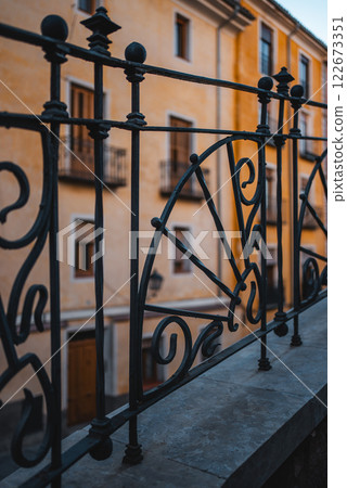 Intricate ironwork adorns the balcony railing, framing the view historic buildings and charming streets, showcasing its rich architectural heritage Intricate ironwork adorns the balcony railing, framing the view historic buildings and charming streets, showcasing its rich architectural heritage 122673351