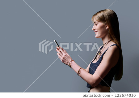 Fashionable young woman using smartphone, profile view, gray background 122674030