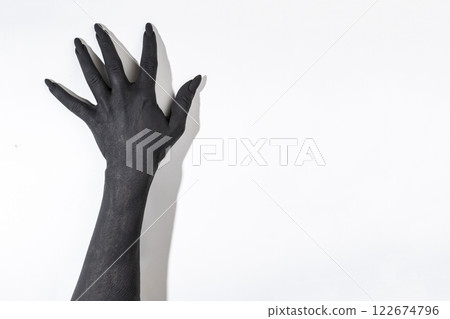 The black hand with long nails. Concept photo with woman hand painted in black paint - moving on wall The black hand with long nails. Concept photo with woman hand painted in black paint - moving on wall 122674796