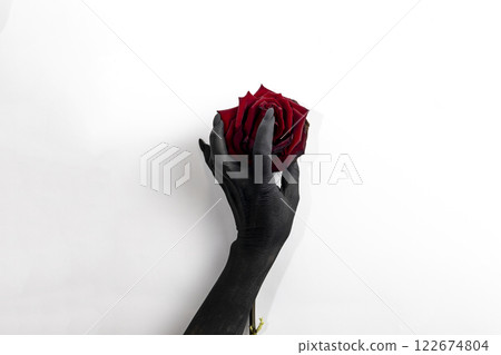 The black hand with long nails hold a rose and make it dry. Concept photo with woman hand painted in black paint with hold a red flower. Demon power in hand make rose die 122674804