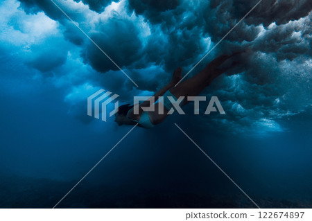 Woman in bikini dive without surf board under ocean wave. Duck dive under crashing wave 122674897