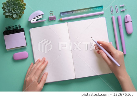 Blank notepad page for your text in a pastel colored stationery frame. Woman's hands are holding a pen. Background in mint green color. Blank notepad page for your text in a pastel colored stationery frame. Woman's hands are holding a pen. Background in mint green color. 122676163