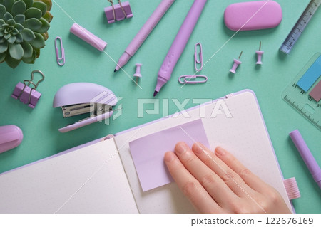 Female hand sticking purple sticker to notebook page. Stationery background, pastel colors. Place for your text. Female hand sticking purple sticker to notebook page. Stationery background, pastel colors. Place for your text. 122676169