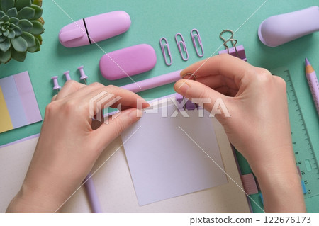 Blank notepad page for your text in pastel colored stationery frame. A woman attaches a note with a paperclip. Background in mint green color. Blank notepad page for your text in pastel colored stationery frame. A woman attaches a note with a paperclip. Background in mint green color. 122676173