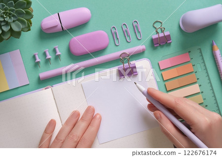 Blank notepad page for your text in pastel colored stationery frame. A woman writes with a pen on a sticker. The background is mint green color. 122676174