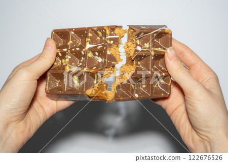 Close up of famous Dubai chocolate with peanut butter, caramel and kadaif broken in woman's hands. Confectionery handmade sweets, chocolatier Close up of famous Dubai chocolate with peanut butter, caramel and kadaif broken in woman's hands. Confectionery handmade sweets, chocolatier 122676526