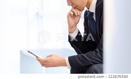 男商人一邊看著智慧型手機一邊思考 122676580