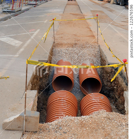 Street repair in progress with new communication pipes being laid in a dug trench during daytime construction 122676596