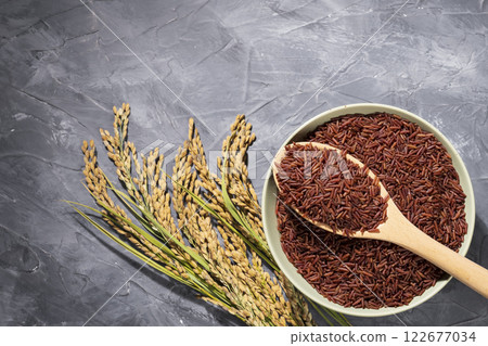Red-rice in a bowl with wooden spoon and ears of rice on gray table Red-rice in a bowl with wooden spoon and ears of rice on gray table 122677034