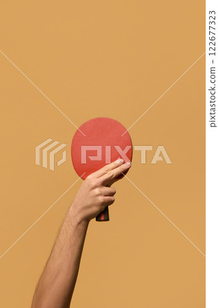 Hand gripping red table tennis paddle with firm hold, showcasing agility and strategy in fast-paced gameplay against solid beige background. Hand gripping red table tennis paddle with firm hold, showcasing agility and strategy in fast-paced gameplay against solid beige background. 122677323