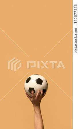 Outstretched arm holding leather soccer ball against beige background, showcasing preparation to serve, to start powerful game. 122677336