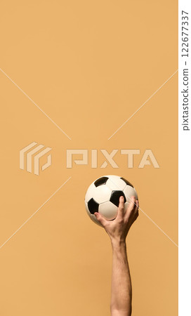 Hand gripping soccer ball high, fingers pressing against black-and-white panels, representing strength, control, and energy essential for competitive play. Hand gripping soccer ball high, fingers pressing against black-and-white panels, representing strength, control, and energy essential for competitive play. 122677337