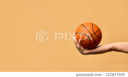 Arm extended outward, gripping basketball firmly, demonstrating stability, technique, and readiness to make powerful play against warm-toned background. 122677345