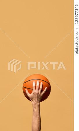 Hand pressing fingers on basketball, showcasing grip, precision, and strength, ready for dynamic movement and control in game against warm-toned background. 122677346