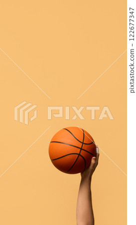 Hand gripping basketball from below, prepared for dynamic movement, highlighting skill and agility in sports against warm-toned background. 122677347