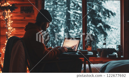 Male freelancer working remotely at a laptop sitting in a country house, cabin, cottage in the winter season. Remote work in cold festive season. This is AI-generated item 122677692