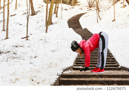 Woman wearing sportswear exercising outside during winter Woman wearing sportswear exercising outside during winter 122678075