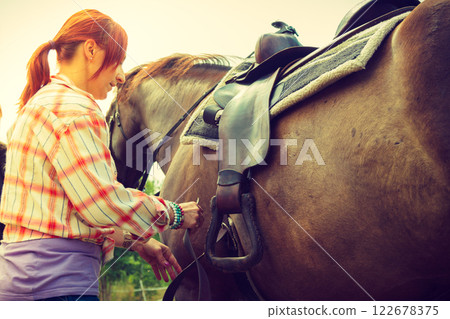 Cowgirl getting horse ready for ride on countryside 122678375