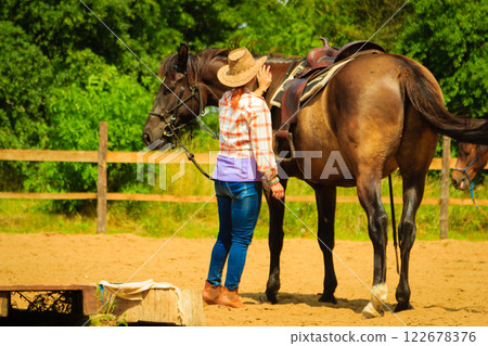 Cowgirl getting horse ready for ride on countryside 122678376
