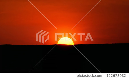 Bright orange sun setting behind dark hills 122678982