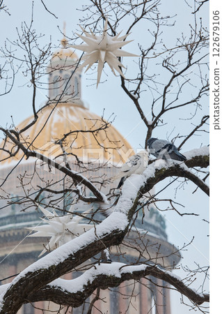 a snow-covered New Year's city decorated for the celebration of the new year, pigeons on a tree, the golden dome of St. Isaac's Cathedral 122679106
