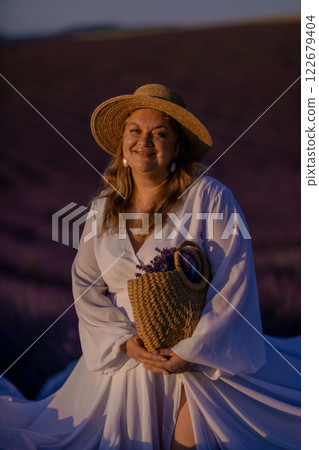 woman poses in lavender field at sunset. Happy woman in white dress holds lavender bouquet. Aromatherapy concept, lavender oil, photo session in lavender 122679404