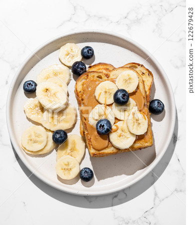 Peanut butter toast on a plate with banana and blueberry on a marble background with shadow. Peanut butter toast on a plate with banana and blueberry on a marble background with shadow. 122679428