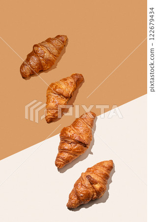 Fresh croissants lie diagonally on orange and white background with shadow. Fresh croissants lie diagonally on orange and white background with shadow. 122679434