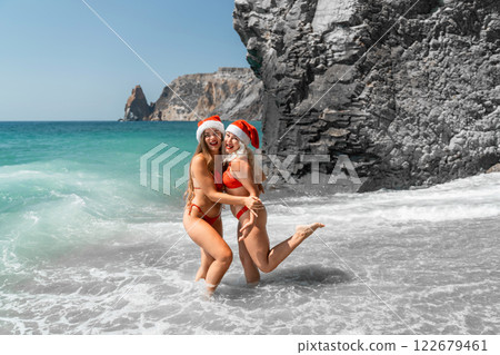 Women in Santa Claus hats run into the sea dressed in red swimsuits. Celebrating the New Year in a hot country 122679461