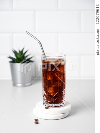 Cold brew coffee in a glass with ice and straw on a light table against a white brick background 122679618