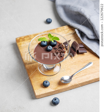 Chocolate pudding in a glass with fresh blueberries and mint on a wooden board on a light background 122679622